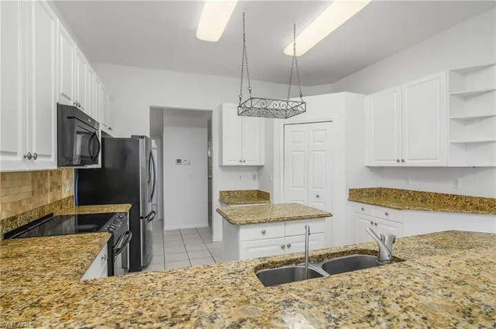 Kitchen with sink, white cabinets, black appliances, and light tile patterned floors