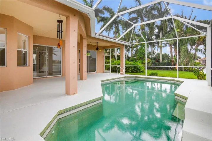 View of swimming pool featuring a patio, ceiling fan, and glass enclosure