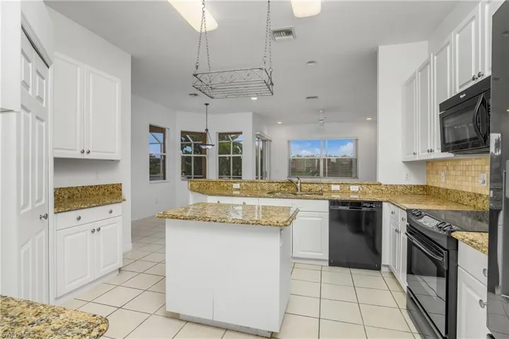 Kitchen featuring black appliances, light stone counters, kitchen peninsula, a center island, and white cabinetry