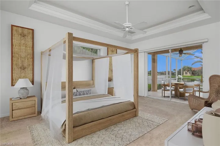 Bedroom featuring light colored carpet, a raised ceiling, multiple windows, and ceiling fan