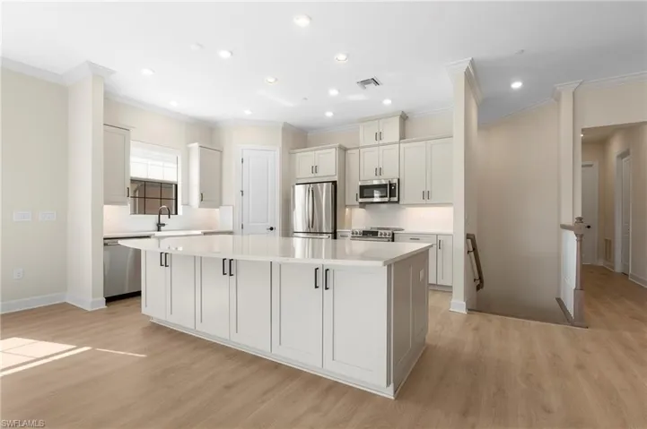 Kitchen with light countertops, a spacious island, appliances with stainless steel finishes, visible vents, and light wood-style floors