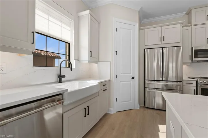 Kitchen featuring crown molding, backsplash, a sink, light wood-style flooring, and appliances with stainless steel finishes
