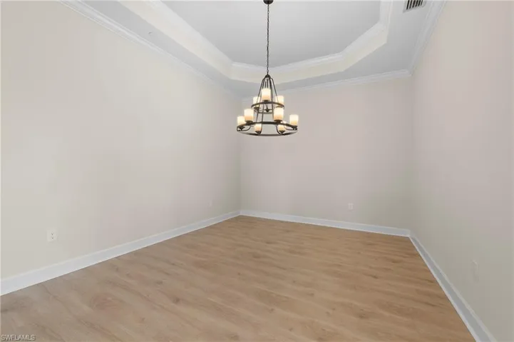 Unfurnished room featuring light wood-type flooring, ornamental molding, baseboards, a chandelier, and a raised ceiling