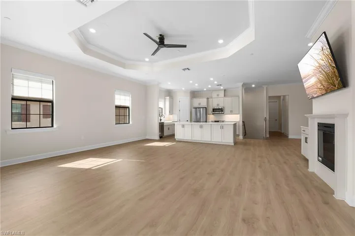 Unfurnished living room with a raised ceiling, a glass covered fireplace, baseboards, light wood-style floors, and ceiling fan