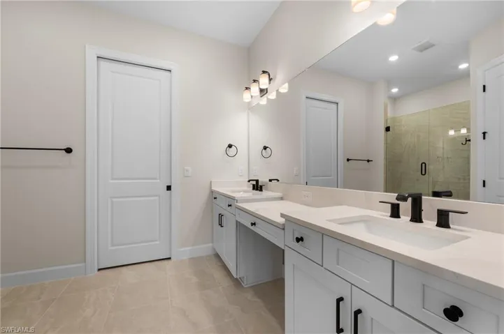 Full bath with a shower stall, double vanity, baseboards, and a sink