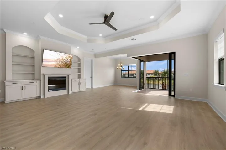 Unfurnished living room featuring a raised ceiling, built in features, and light wood finished floors