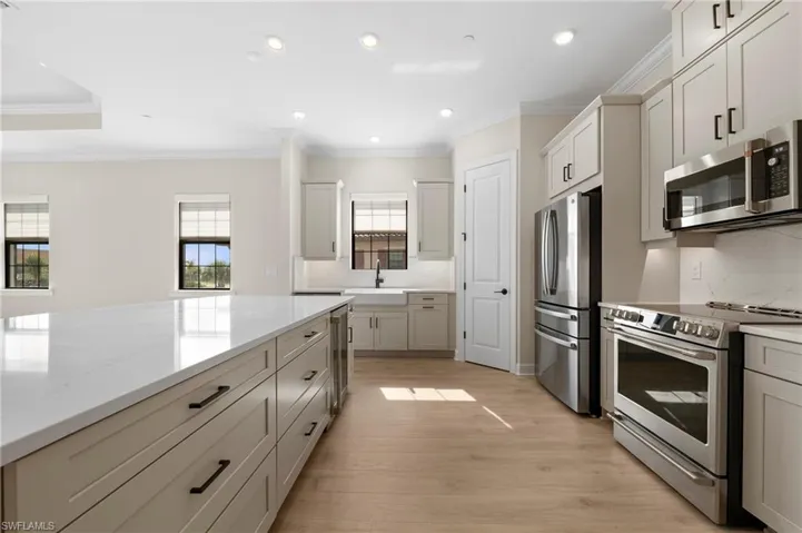 Kitchen with light stone counters, appliances with stainless steel finishes, light wood-style floors, ornamental molding, and recessed lighting