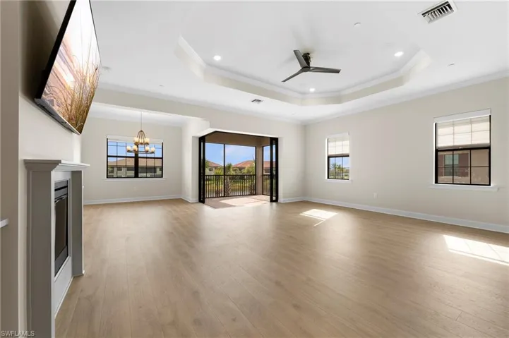 Unfurnished living room with a tray ceiling, ceiling fan with notable chandelier, visible vents, and light wood finished floors