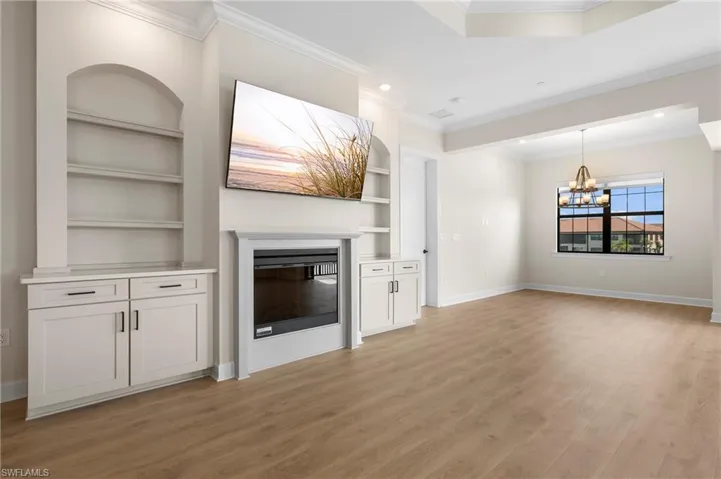 Unfurnished living room with baseboards, built in shelves, light wood-style flooring, a notable chandelier, and a glass covered fireplace