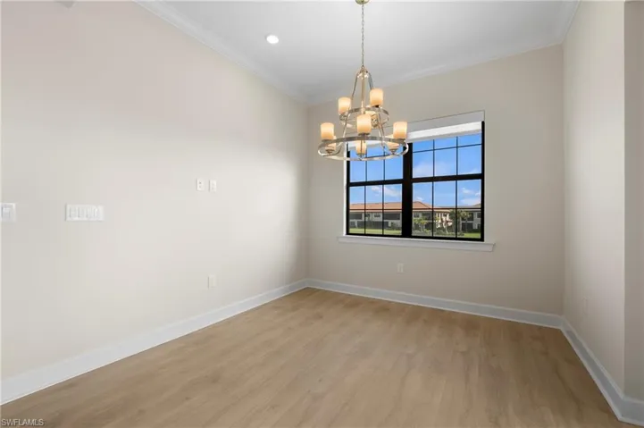 Empty room featuring light wood-style floors, a notable chandelier, crown molding, and baseboards