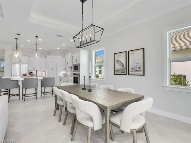 Dining space featuring healthy amount of natural light, crown molding, a chandelier, light tile patterned floors, and a tray ceiling
