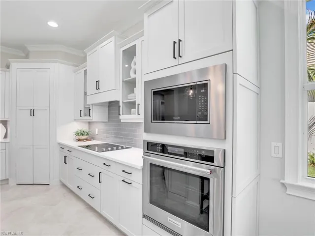 Kitchen featuring crown molding, stainless steel appliances, white cabinetry, backsplash, and glass insert cabinets