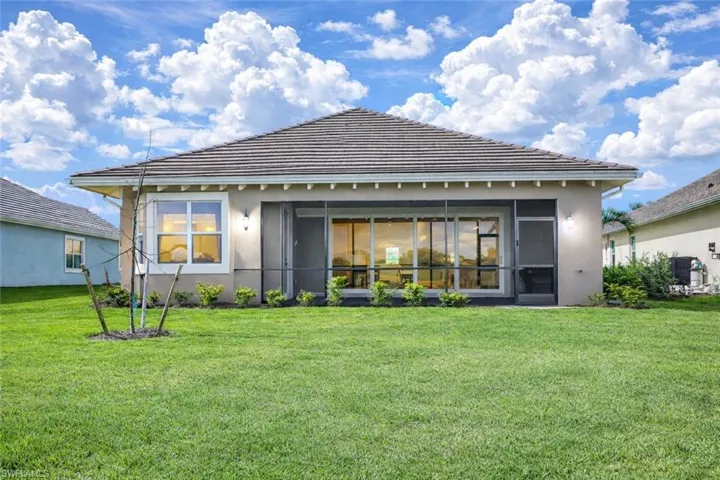 Rear view of house with stucco siding, a sunroom, a lawn, and a tiled roof