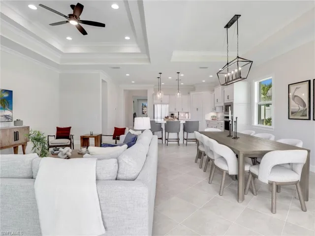 Living area featuring a ceiling fan, a tray ceiling, light tile patterned floors, crown molding, and hanging lights