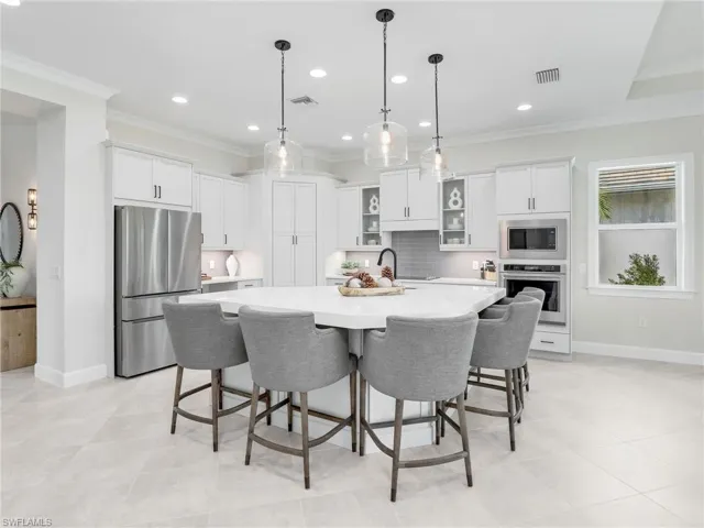 Kitchen with stainless steel appliances, glass insert cabinets, white cabinets, a large island with sink, and hanging light fixtures