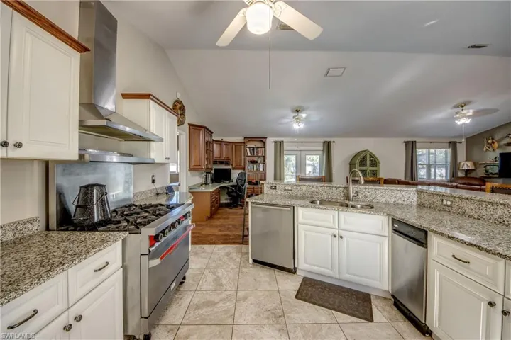 Kitchen with appliances with stainless steel finishes, wall chimney exhaust hood, a sink, a ceiling fan, and lofted ceiling