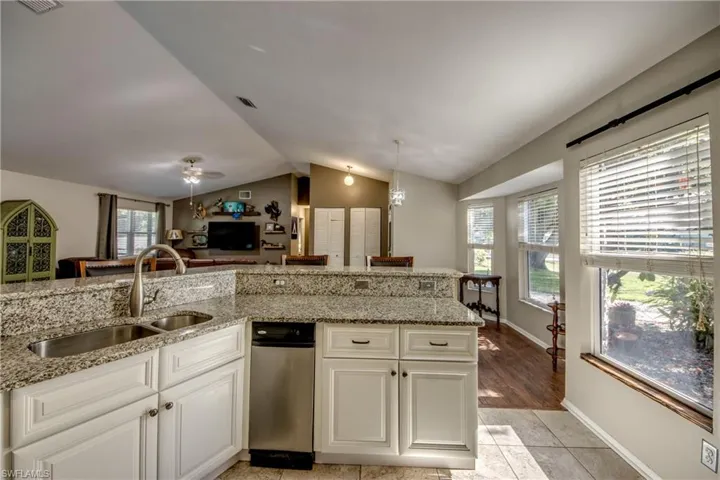 Kitchen with a sink, lofted ceiling, light stone counters, open floor plan, and white cabinetry