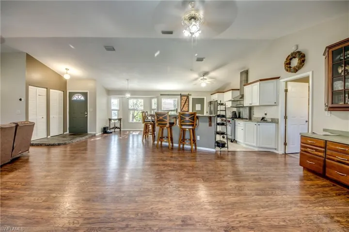 Kitchen featuring a ceiling fan, vaulted ceiling, open floor plan, dark wood finished floors, and glass insert cabinets