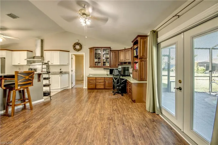 Office area featuring a ceiling fan, built in desk, lofted ceiling, dark wood-style flooring, and french doors