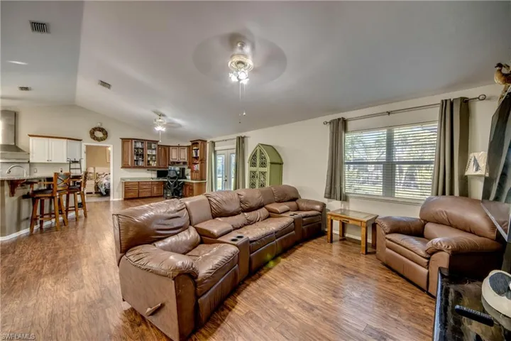 Living room with ceiling fan, wood finished floors, healthy amount of natural light, and lofted ceiling