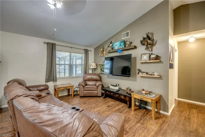Living room with vaulted ceiling, wood finished floors, a ceiling fan, and baseboards