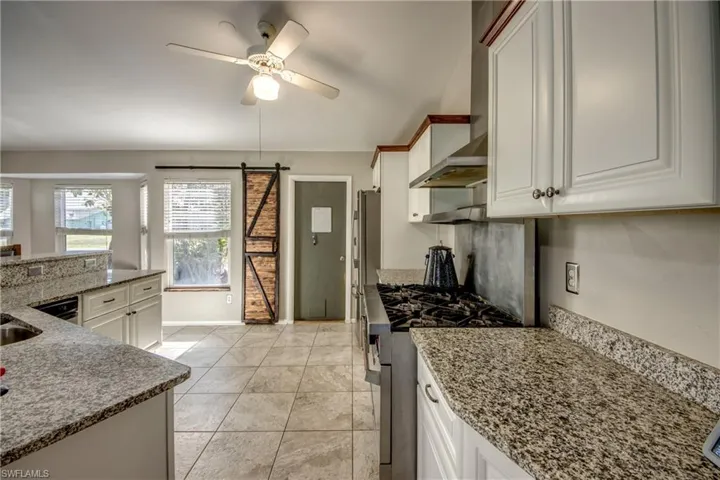 Kitchen featuring stainless steel stove, ceiling fan, a barn door, stone countertops, and white cabinets