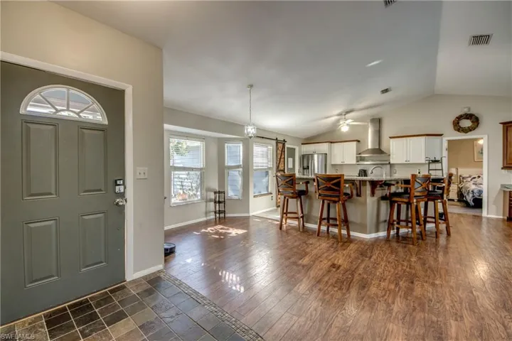Kitchen with wall chimney exhaust hood, stainless steel refrigerator with ice dispenser, a breakfast bar, vaulted ceiling, and ceiling fan