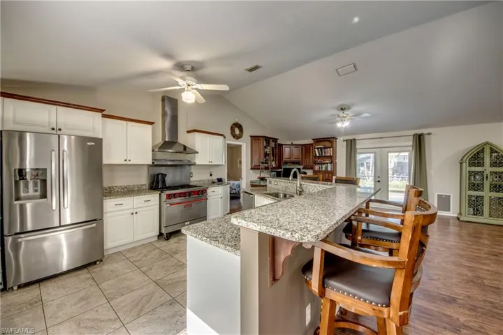 Kitchen with appliances with stainless steel finishes, wall chimney range hood, a ceiling fan, lofted ceiling, and a sink