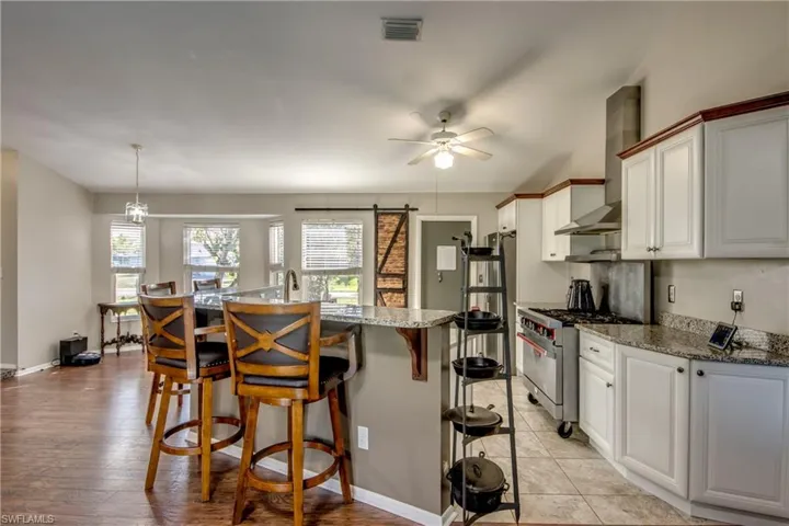 Kitchen with stainless steel stove, wall chimney range hood, a kitchen breakfast bar, a ceiling fan, and light stone counters