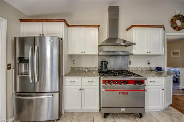 Kitchen featuring stainless steel appliances, wall chimney exhaust hood, light stone counters, and white cabinetry