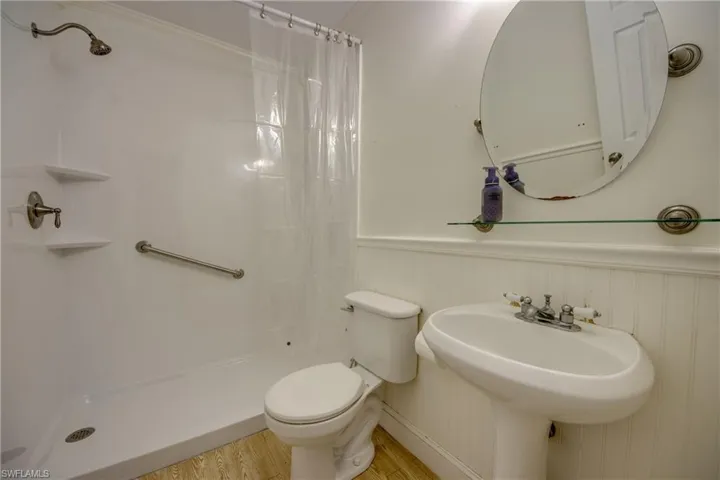 Bathroom with a stall shower, wood finished floors, toilet, wainscoting, and a sink