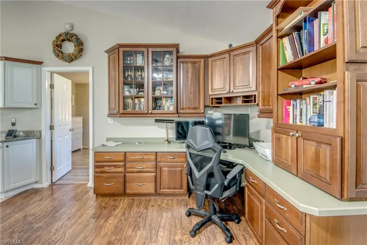 Home office with lofted ceiling, light wood finished floors, and built in desk