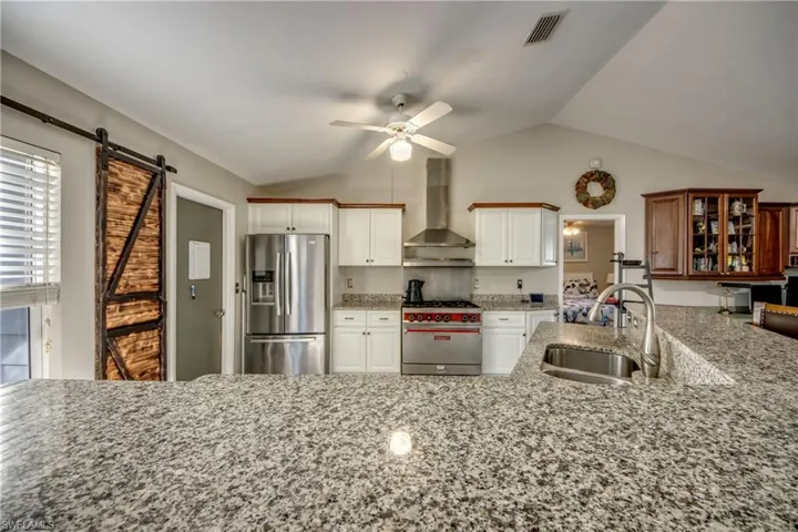 Kitchen with stainless steel fridge with ice dispenser, wall chimney range hood, a sink, range with gas cooktop, and a barn door