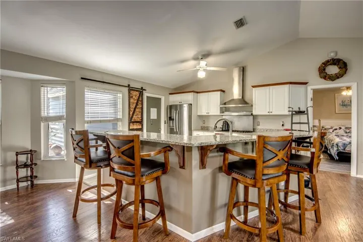 Kitchen featuring stainless steel fridge with ice dispenser, wall chimney range hood, vaulted ceiling, ceiling fan, and dark wood-type flooring
