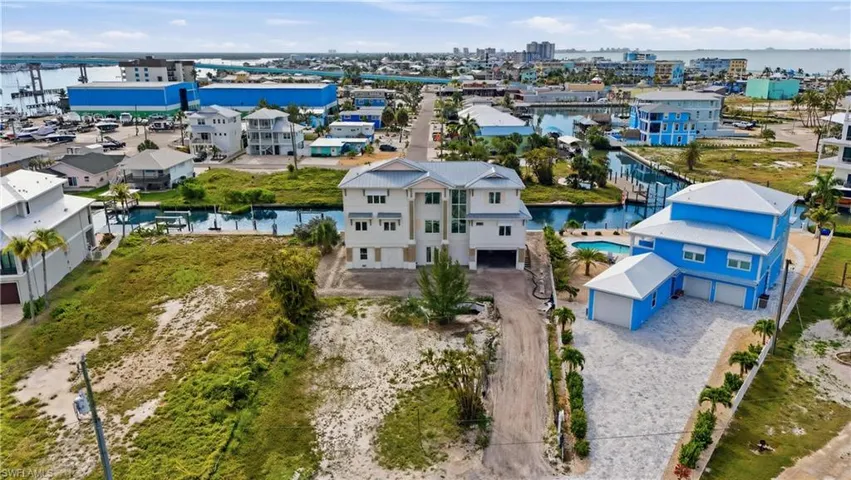 Waterfront property featuring a three-story residence with a multi-car garage, a paver driveway, and an outdoor swimming pool - Virtually Edited Image