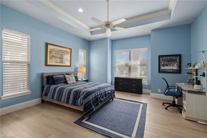 Bedroom with a tray ceiling, ceiling fan, light hardwood / wood-style flooring, and crown molding