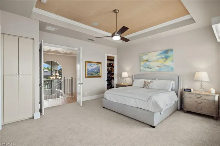 Bedroom with ceiling fan, ornamental molding, light carpet, and a tray ceiling