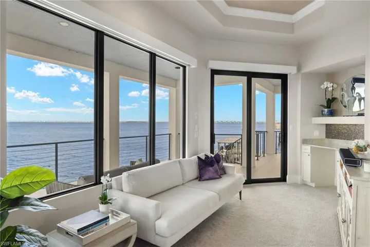 Living room featuring a healthy amount of sunlight, a water view, light colored carpet, and ornamental molding