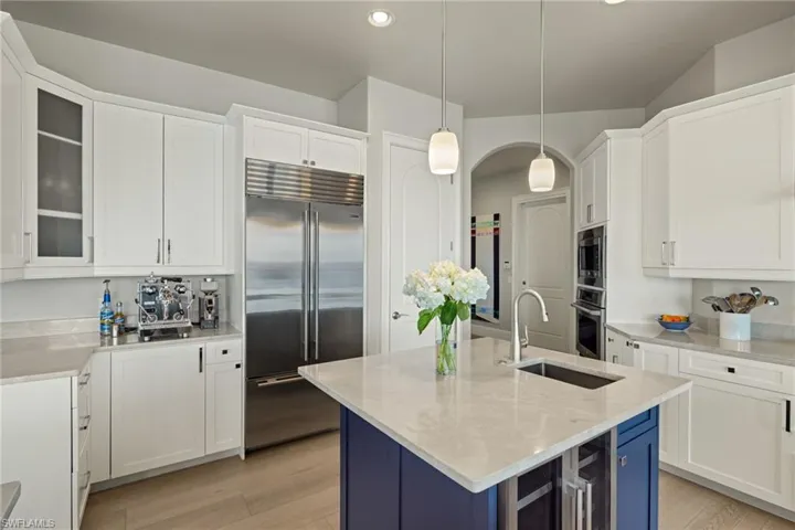 Kitchen with built in appliances, decorative light fixtures, light wood-type flooring, and an island with sink