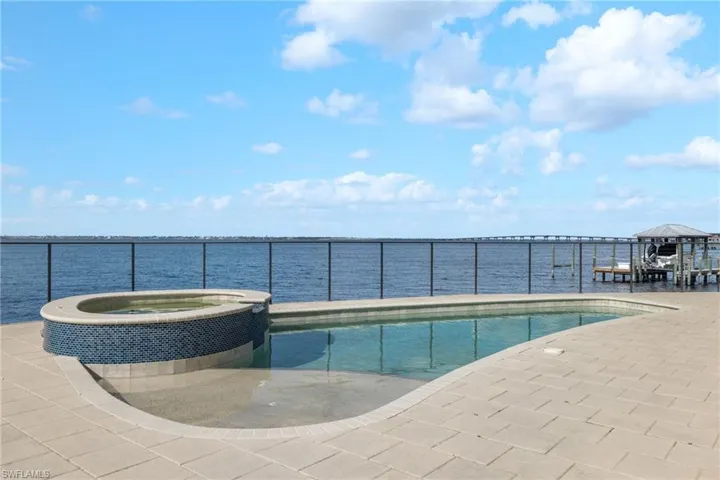 View of swimming pool with an in ground hot tub and a water view