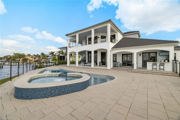 Rear view of house with a water view, a swimming pool with hot tub, a balcony, a patio area, and a bar