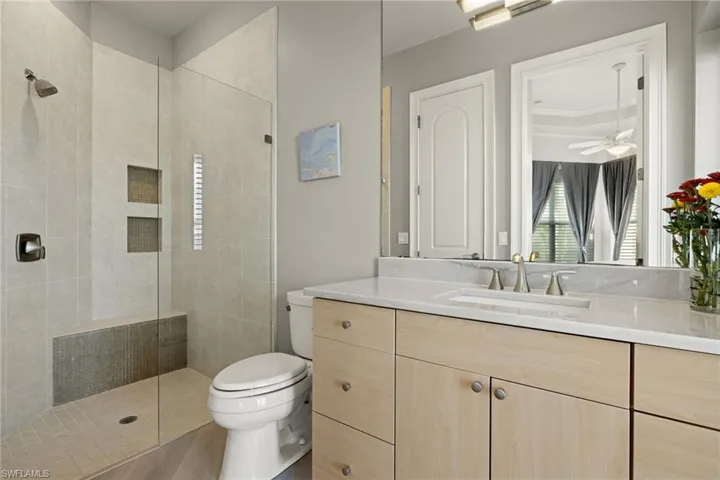 Bathroom with ceiling fan, wood-type flooring, tiled shower, toilet, and vanity