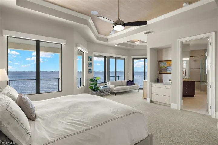 Bedroom featuring connected bathroom, a water view, ceiling fan, and a tray ceiling