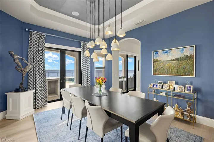 Dining area with french doors, light hardwood / wood-style floors, a tray ceiling, a water view, and ornamental molding