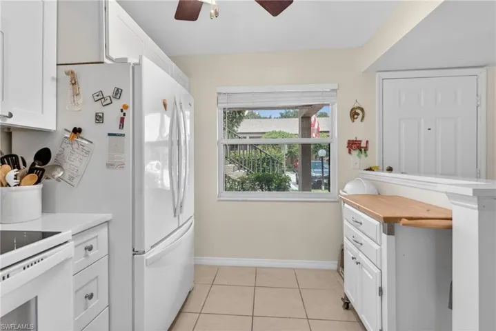 Functional kitchen featuring white cabinetry with silver hardware, white appliances, a window with horizontal blinds, and ceramic tile flooring