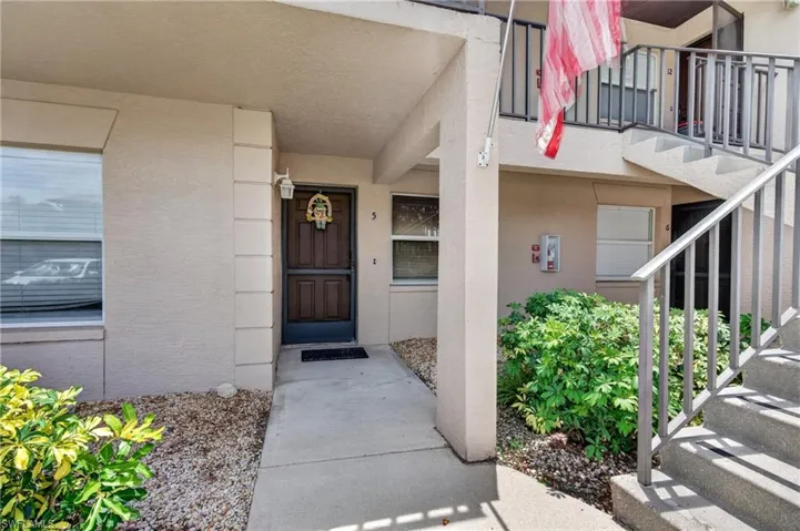 Ground-floor entryway featuring a paneled door, exterior wall lantern, and concrete walkway
