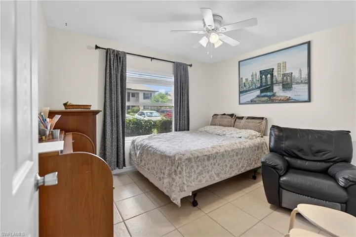 Bedroom featuring light tile flooring, a window with dark curtains, and a ceiling fan with integrated lighting