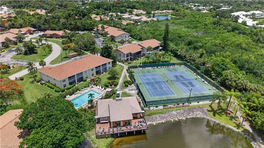 Aerial perspective showcasing multiple buildings, a swimming pool, two tennis courts, and a waterfront deck
