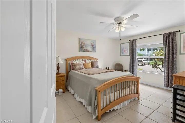 Spacious bedroom featuring light-toned tile flooring, a window with exterior views, and a ceiling fan with integrated lighting
