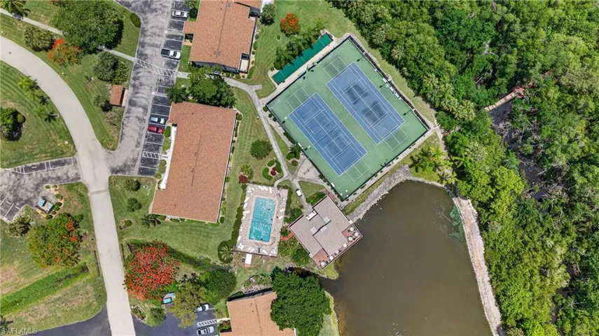 Aerial view showcasing the property's amenities, including two tennis courts, a swimming pool, and a waterfront building with an outdoor deck